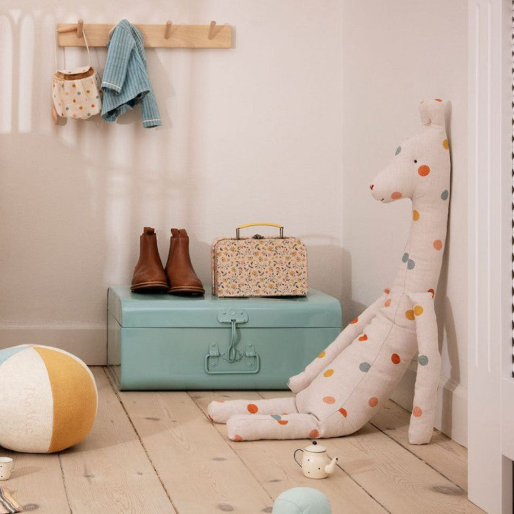 Maileg big white giraffe stuffed toy with colorful polkadots sitting in a playroom with toys.