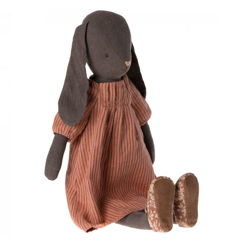 Dark brown Maileg rabbit sitting down and wearing a reddish striped dress.