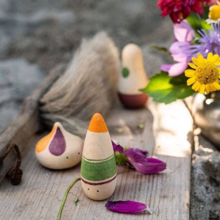 3 Wooden Humanoid Figures outsides on a wooden plank near a small bouquet of flowers